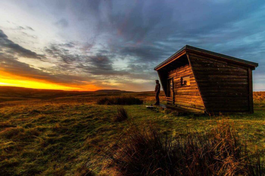 Man standing outside tiny house at sunrise - tiny flat pack houses you can build yourself