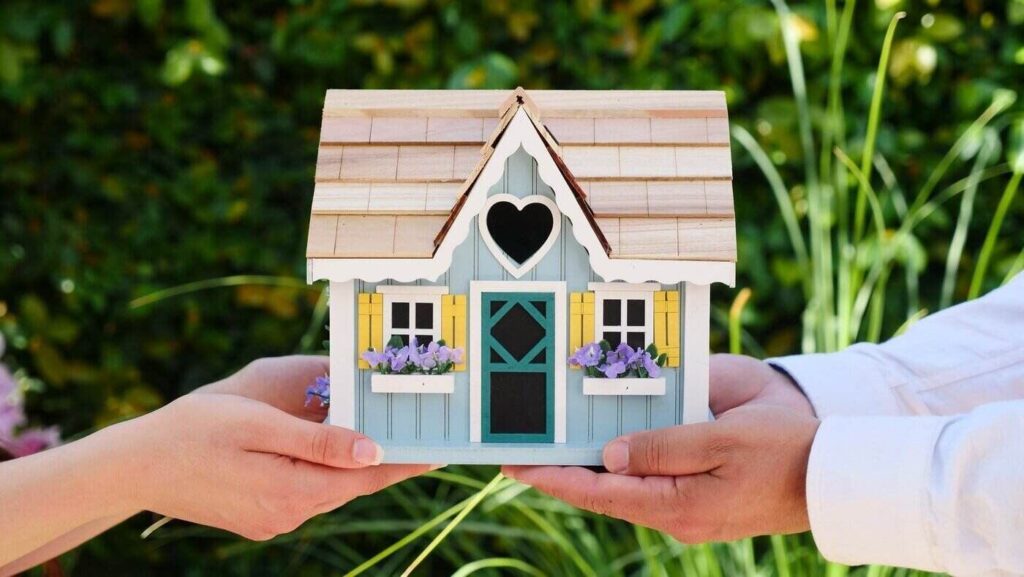 Two people holding small wooden house - keep these 6 things in mind when looking for a green home