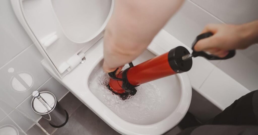 Emergency Maintenance: How To Handle Urgent Repairs Effectively 4 Man unclogging toilet with auger
